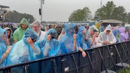 Menschen mit Regenponchos stehen beim Hurricane Festival in Scheeßel hinter einer Absperrung. © NonstopNews 