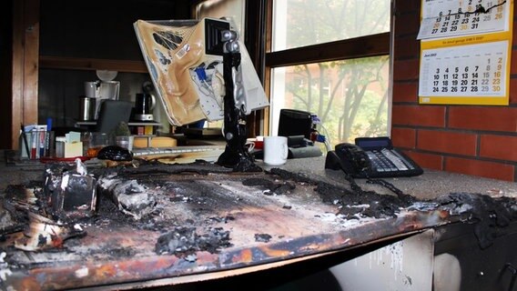 Ein vom Feuer geschädigter Schreibtisch. Telefon, PC-Monitor und diverse Utensilien sind zum Teil geschmolzen. © NDR Foto: Ann-Kristin Mennen