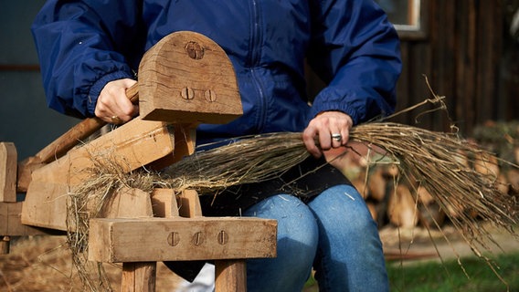 Ein Bündel Flachsstängel werden mit einem Holzgerät gebrochen. © Landkreis Lüchow-Dannenberg/Ulrike Kohn Foto: Ulrike Kohn/Landkreis Lüchow-Dannenberg