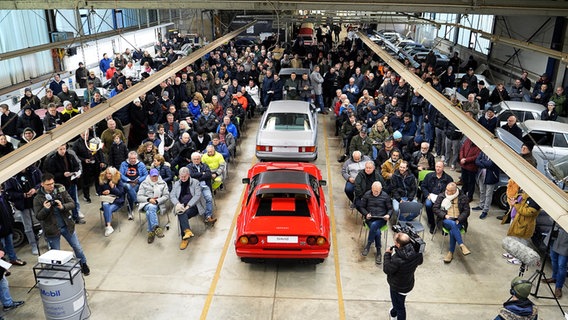 Zahlreiche Menschen nehmen an einer Auktion von Oldtimern im Landkreis Harburg in einer Halle teil. © dpa Foto: Jörn Hüneke