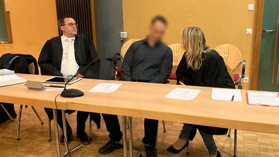 Ein Angeklagter sitzt in einem Gerichtssaal neben seinen Verteidigern. © NDR Foto: Maren Momsen