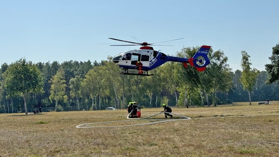 Einsatzkräfte der Feuerwehr befestigen während einer Übung einen Löscheimer an einem Hubschrauber. © NDR Foto: Regina Hamborg