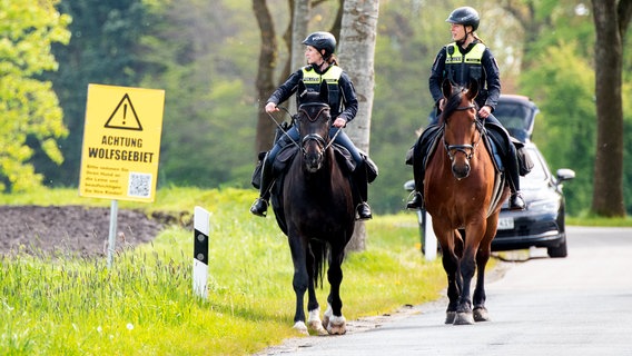 Der sechs Jahre alte Arian aus Elm wird weiter vermisst. Zwei Polizistinnen auf Pferden suchen nach einem vermissten Jungen und reiten dabei an einem Schild mit der Aufschrift "Achtung Wolfsgebiet!" vorbei. © dpa Bildfunk Foto: Daniel Bockwoldt