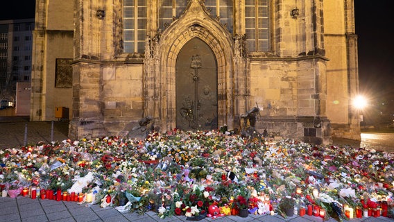 Zahlreiche Kerzen, Blumen und Kränze liegen beziehungsweise stehen vor dem Eingang der Johanniskirche in Magdeburg. © dpa-Bildfunk Foto: Sebastian Kahnert