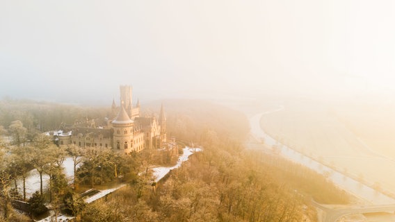 Bei Temperaturen unter dem Gefrierpunkt taucht die aufgehende Sonne das Schloss Marienburg in der Region Hannover in goldenes Licht. © dpa Foto: Julian Stratenschulte