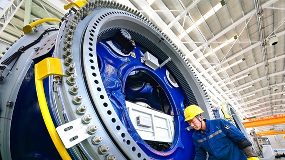 Ein Mann mit Helm und in Arbeitskleidung putzt ein Bauteil eines Windrades. © picture alliance / CFOTO | CFOTO 