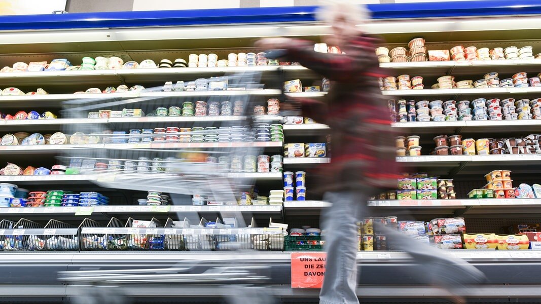 Eine Kundin geht in einem Supermarkt mit ihrem Einkaufswagen an einem Kühlregal vorbei.