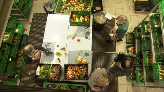 Drei Ehrenamtliche helfen bei der Tafel mit, Lebensmittel herzurichten. © NDR Foto: NDR