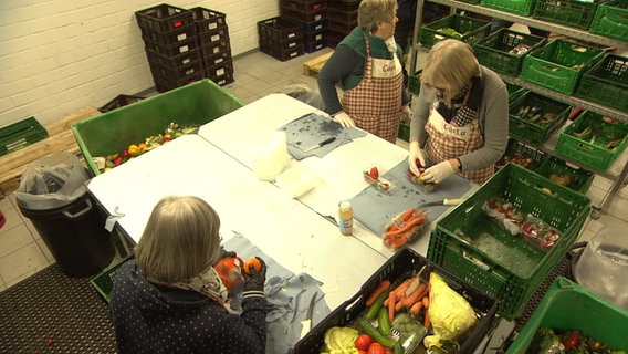 Drei Ehrenamtliche helfen bei der Tafel mit, Lebensmittel herzurichten. © NDR Foto: NDR