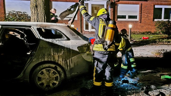 Feuerwehrleute stehen mit Atemschutzgeräten an einem ausgebrannten Auto © Pressestelle Feuerwehr Verden 