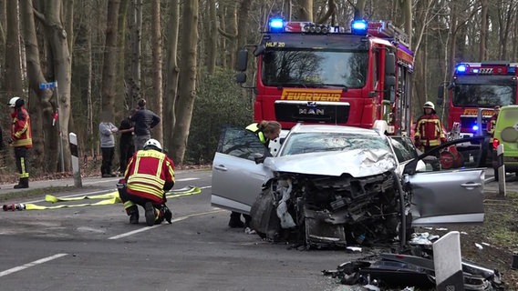 Nach einem Unfall steht ein stark beschädigtes Auto auf einer Straße, Einsatzkräfte sind ebenfalls vor Ort. © NonstopNews 