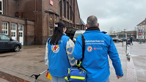 Vor dem Oldenburger Bahnhof stehen zwei Mitarbeiter der Bahnhofsmission in ihren blauen Westen. © NDR Foto: Pascal Klug