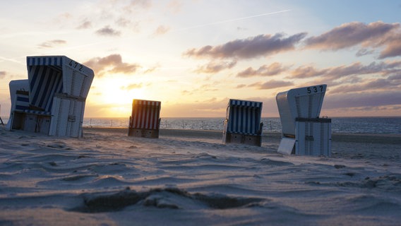 Vier Strandkörbe stehen am Strand von Baltrum und im Hintergrund geht die Sonne unter. © dpa Foto: Anja Dembski