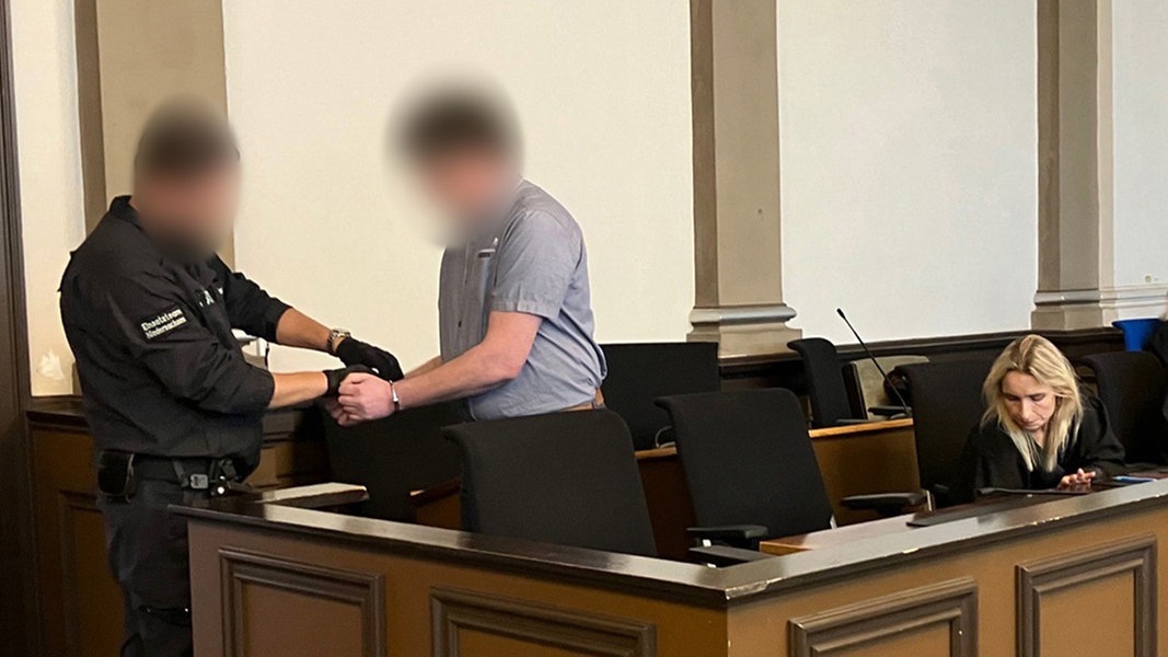 Ein Justizvollzugsbeamter legt einem Angeklagten Handschellen an.