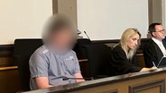 Ein Angeklagter sitzt neben seinen Anwälten in einem Gerichtssaal. © NDR Foto: Maren Momsen