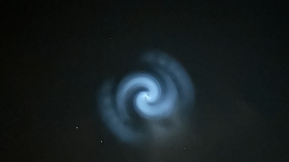 Am Abendhimmel zeigt sich eine blau leuchtende Spirale. © NDR Foto: Kerstin Stüvecke