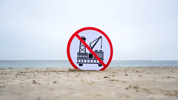 Auf einem Schild am Strand ist eine Bohrinsel durchgestrichen. © dpa Foto: Sina Schuldt