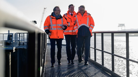 Holger Banik (l-r), Geschäftsführer Niedersachsen Ports GmbH, Olaf Lies (SPD), Wirtschaftsminister von Niedersachsen, und Stefan Wenzel (Bündnis 90/Die Grünen), Parlamentarischer Staatssekretär des Bundesministeriums für Wirtschaft und Klimaschutz, gehen zusammen auf einem Anleger. © Philipp Schulze/dpa Foto: Philipp Schulze