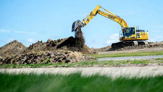 Ein Bagger steht auf einem Deichabschnitt und kippt mit seiner Schaufel Erde ab. © dpa-Bildfunk Foto: Hauke-Christian Dittrich/dpa