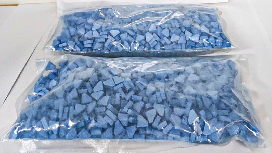Plastikbeutel mit blauen Ecstasy-Pillen liegen auf einem Tisch.