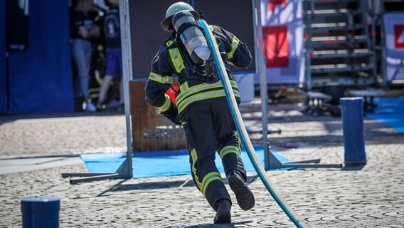 Ein Feuerwehrmann sprintet bei der Firefighter Combat Challenge in Bremerhaven mit einem Schlauch zum Brandort. © dpa-Bildfunk Foto: Focke Strangmann