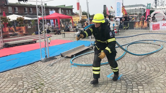 Ein Feuerwehrmann trägt bei der Firefighter Combat Challenge in Bremerhaven einen schweren Schlauch. © NDR Foto: Catherine Grim