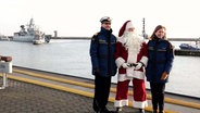 Ein Weihnachtsmann steht zusammen mit Angehörigen der Marine beim Eintreffen der Fregatte "Hamburg" am Hafen. © Nord-West-Media TV 