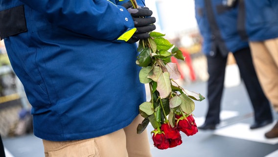 Angehörigen begrüßen die Besatzung der "Hamburg" und eine Person hält dabei rote Rosen hinter dem Rücken. © dpa-Bildfunk Foto: Sina Schuldt