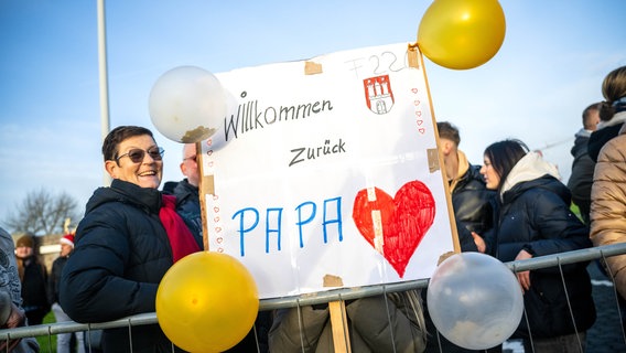 Angehörigen warten mit Plakaten am Pier des Marinestützpunktes in Wilhelmshaven auf die "Hamburg". © dpa-Bildfunk Foto: Sina Schuldt