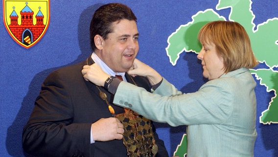 2002: Die CDU-Vorsitzende Angela Merkel überreicht Niedersachsens Ministerpräsident Sigmar Gabriel (SPD) in Berlin die Insignien des Grünkohl-Königs. Sie war seine Vorgängerin als Grünkohl-Königin. © picture-alliance / dpa/dpaweb | Marcel_Mettelsiefen Foto: Marcel Mettelsiefen