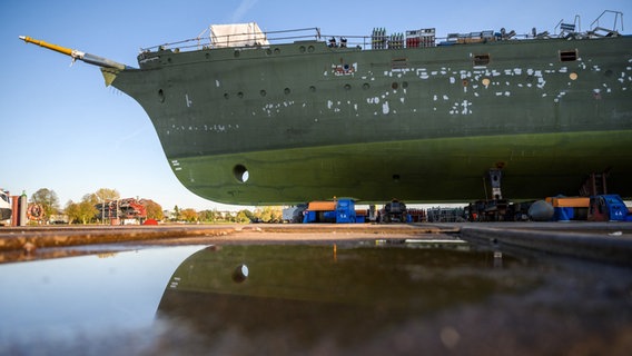 Das teilsanierte Marineschulschiff Gorch Fock liegt kurz vor der Schleppfahrt zur Lürssen-Werft am Gelände der Fassmer-Werft und spiegelt sich in einer Pfütze. © dpa Foto: Mohssen Assanimoghaddam