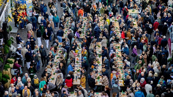 Zahlreiche Besucher sitzen auf dem Rathausmarkt an langen Tischreihen und essen Grünkohl. © dpa Foto: Hauke-Christian Dittrich