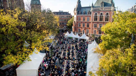 Zahlreiche Besucher sitzen auf dem Oldenburger Rathausmarkt an langen Tischreihen und essen Grünkohl. © picture alliance/dpa | Hauke-Christian Dittrich Foto: Hauke-Christian Dittrich