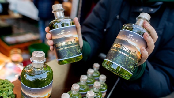 Sina hält am Stand von "Bastwöste & Co" auf dem Rathausmarkt zwei Flaschen Grünkohl-Gin in den Händen. © dpa Foto: Hauke-Christian Dittrich