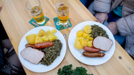 Zwei Teller mit einer Portion Grünkohl und den Beilagen Salzkartoffeln, Kochwurst, Pinkelwurst und Kasseler stehen auf einem Tisch auf dem Rathausmarkt. © dpa Foto: Hauke-Christian Dittrich