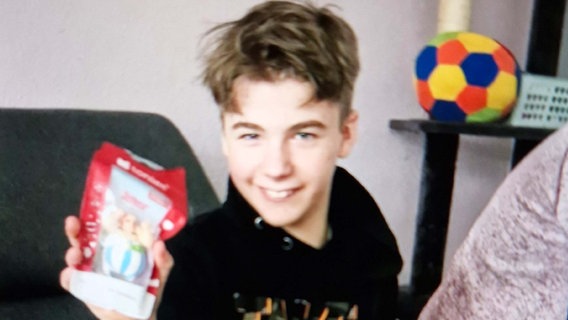 Der vermisste 13-jährige Jeremy Jason H. sitzt auf einem Sofa, hält ein Spielzeug in der Hand und lächelt in die Kamera. © Polizeiinspektion Cuxhaven 