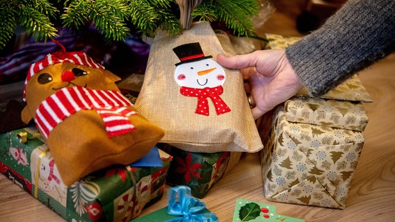 Eine junge Frau legt an Heiligabend mehrere Geschenke unter einen Weihnachtsbaum. © dpa Foto: Hauke-Christian Dittrich