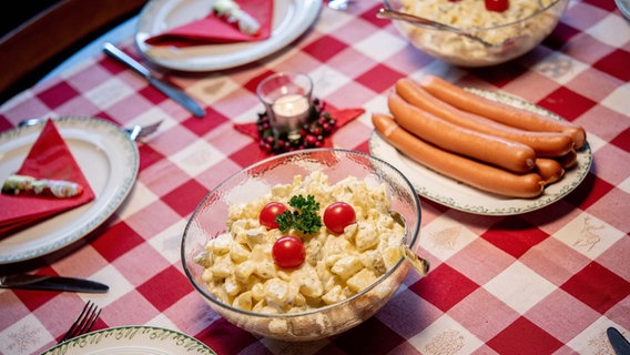 Würstchen und Kartoffelsalat stehen an Heiligabend auf einem gedeckten Tisch. © dpa Foto: Hauke-Christian Dittrich