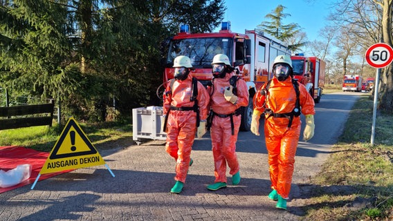 Drei Feuerwehrmänner in Schutzanzügen und mit Atemmaske gehen eine Straße entlang. © Freiwillige Feuerwehr Wiesmoor Foto: Jan-Marco Bienhoff