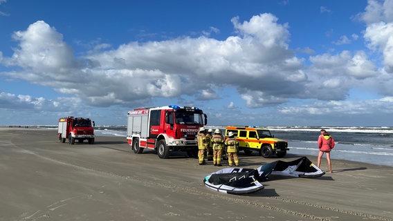 Ein Kite liegt an einem Strand. Dahinter stehen Feuerwehrleute vor einem Löschfahrzeug. © Kreisfeuerwehrverband Aurich Foto: Jacob Habinga