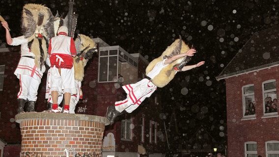 Mit Masken verkleidete Männer stürzen sich am "Klaasohm"-Fest in der Innenstadt der Nordseeinsel Borkum von einer Litfaßsäule in die Arme der Schaulustigen. © picture alliance/dpa/Reinhold Grigoleit Foto: Reinhold Grigoleit