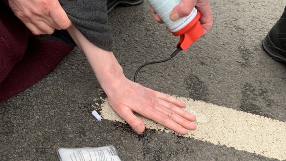 Ein Aktivist der Gruppe "Letzte Generation" hat seine Hand auf eine Straße geklebt. © NDR Foto: Anna Schlieter