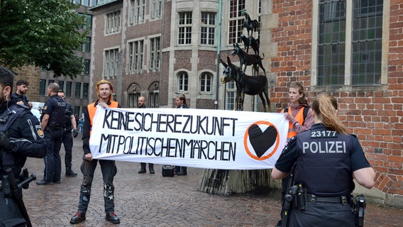 Aktivisten von "Letzte Generation" protestieren mit einem Plakat vor den Bremer Stadtmusikaten. Die Statue ist mit schwarzer Farbe beschmiert. © Letzte Generation 
