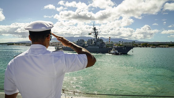 Ein Marinesoldat an Deck salutiert auf Hawaii vor der vorbeifahrenden USS Fitzgerald, einem US Zerstörer der Arleigh Burke Klasse. © Bundeswehr 
