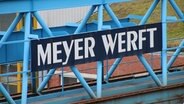 An einem blauen Metallgerüst hängt ein Schild mit der Aufschrift "Meyer Werft". © NDR Foto: Oliver Gressieker