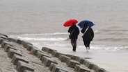 Spaziergängerinnen gehen mit Regenschirmen am Nordstrand der ostfriesischen Insel Norderney bei regnerischem Wetter. © dpa-Bildfunk Foto: Volker Bartels