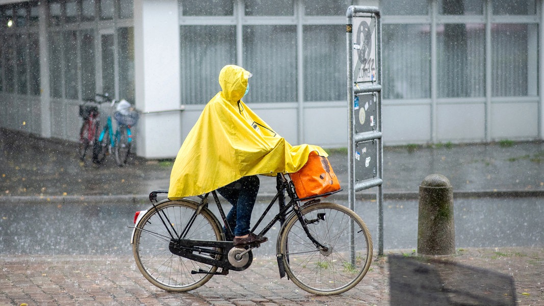 Ein Frau fährt während eines Gewitters mit einem gelben Regenponcho durch Oldenburg.