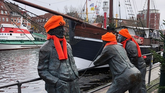 Statuen am Hafen von Emden sind anlässlich des "Orange Day" mit orangen Mützen und Schals bekleidet. © NDR Foto: Regine Schramm