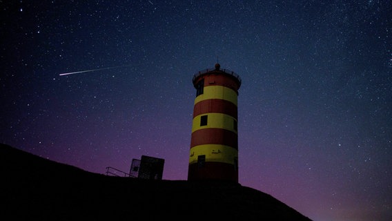 Eine Sternschnuppe leuchtet über der Nordsee am Nachthimmel über dem Pilsumer Leuchtturm. © dpa Foto: Matthias Balk