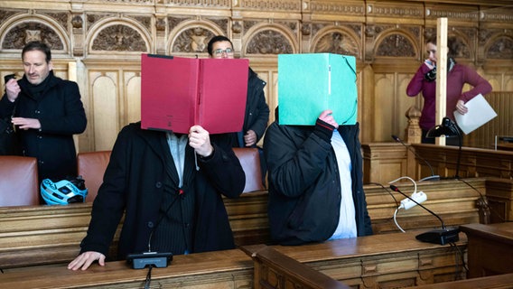 Zwei Angeklagte stehen vor Prozessbeginn im Gerichtssaal des Landgerichts Bremen und verbergen ihre Gesichter. © dpa-Bildfunk Foto: Sina Schuldt
